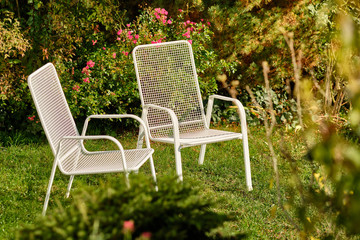 Two white garden chairs are standing in an idyllic green sunny October garden in Germany