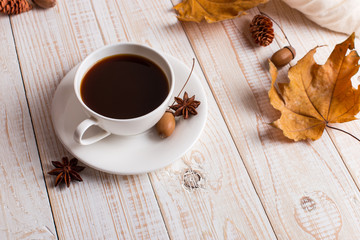 White scarf, cup of coffee and dry yellow leaves on a wooden table. Autumn mood, copy space.