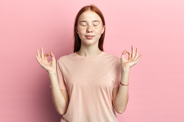 Portrait happy young woman in pink shirt with eyes closed hands raised in air relaxing meditating...