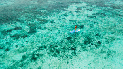 Woman standing on sup board. Background of turquoise transparent water surface over coral reef....