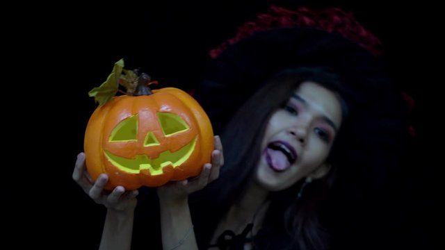 Playful woman in Halloween costume hiding and showing funny face behind Halloween pumpkin or Jack O Lantern 