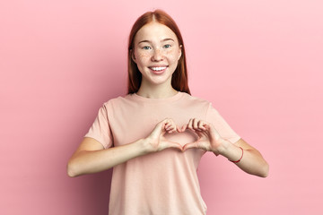 Close up portrait of positive charming girl giving boyfriend her heart isolated pink background,...