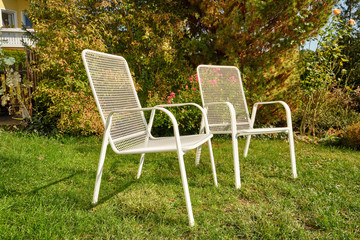 Two white garden chairs are standing in an idyllic green sunny October garden in Germany