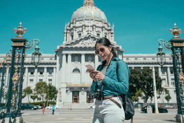 San Francisco city hall is Beaux-Arts architecture and located in city civic center. girl travel backpacker carrying camera and using cellphone searching direction on online map under sunny blue sky