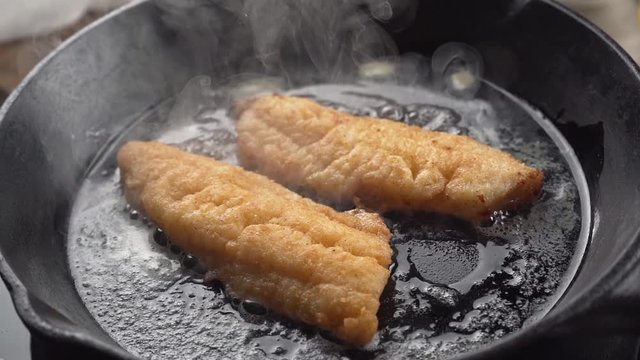 Slow motion of breaded fish fillets frying in butter in a cast iron skillet.