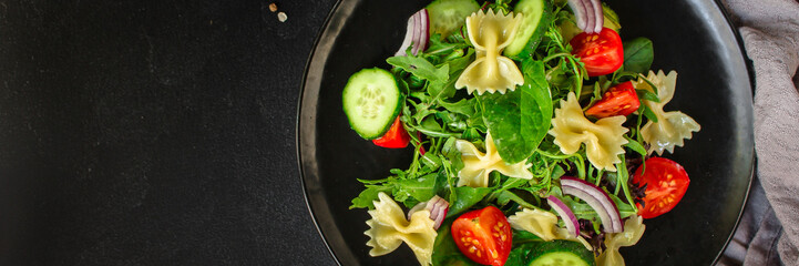 italian pasta salad farfalle, vegetables, mix leaves (tomato, cucumber, onion, lettuce, chard, arugula and more) menu concept. food background. copy space. Top view
