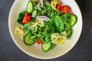 italian pasta salad farfalle, vegetables, mix leaves (tomato, cucumber, onion, lettuce, chard, arugula and more) menu concept. food background. copy space. Top view