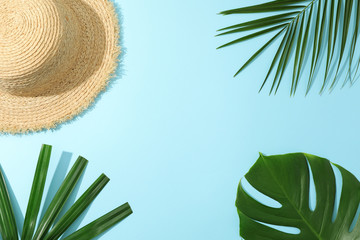Palm leaves and straw hat on blue background, copy space