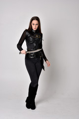 full length portrait of a pretty brunette woman wearing black leather fantasy costume. Standing...