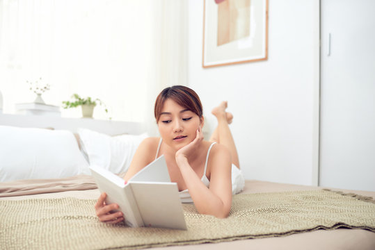 Girl reading a book in bed, lying on bed smiling happy and relaxed.