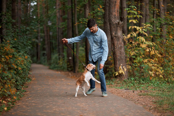 cheerful young man having fun with dog in the autumn forest, friendship, entertainment. full length photo