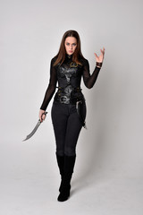 full length portrait of a pretty brunette woman wearing black leather fantasy costume. Standing...