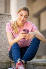 smiling teenager girl sitting outside looking at cellphone