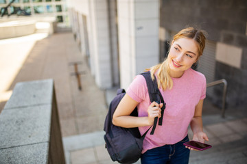 happy teenager student walking outside on campus with mobile phone and bag