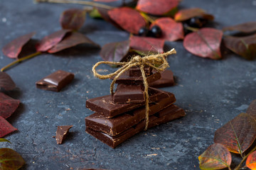 Pieces of dark chocolate and fall leaves on a dark background. Candy sweet dessert and snack. Dark chocolate is an antioxidant and boosts energy and serotonin. Close up, copy space