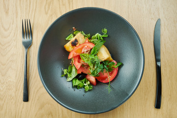 salad with fried halumi cheese cherry tomatoes and microgreen in black bowl on wooden background. Restaurant food