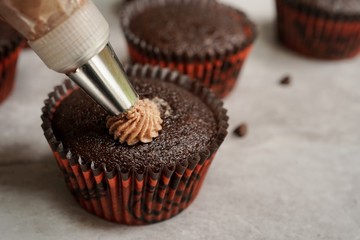 Piping buttercream frosting on chocolate cupcakes, selective focus
