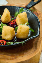 Deep fried crispy Camembert with cranberry sauce in a decorative pan on wooden background. Close up, selecive focus