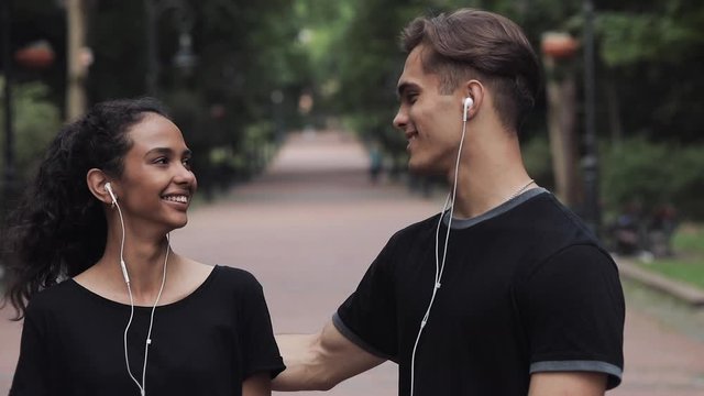 Pretty Musline Girl and Young Man Wearing Headsphones Talking Man Showing Thumb up and Smiling in Park Slow Motion.