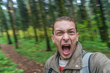 brunette man screaming in the forest in a frightened voice, portrait of a screaming man with his mouth wide open in the autumn forest