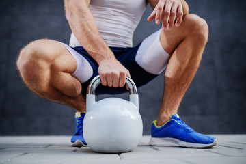 Caucasian sporty muscular man posing, crouching and holding kettle bell outdoors.