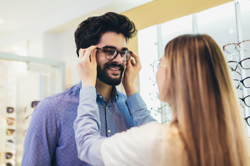 Femaale ophthalmologist helping man to choose glasses in optical store