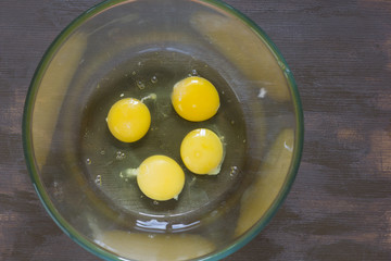 Four raw chicken yolks and whites in glass bowl on the wooden table