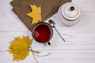 tea in a white cup with white sugar in cubes and cane sugar, maple leaves and apples on a wooden light background.