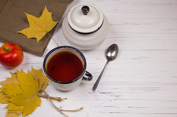 tea in a white cup with white sugar in cubes and cane sugar, maple leaves and apples on a wooden...