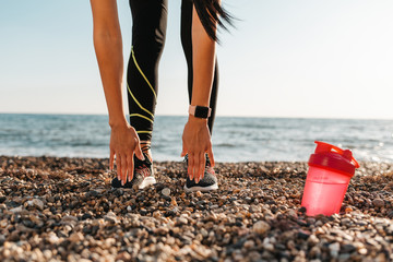 Concept of sport and healthy lifestyle. A woman in sportswear is stretching, a shaker is lying next to her. In the background, the sea and the sky. Copy space
