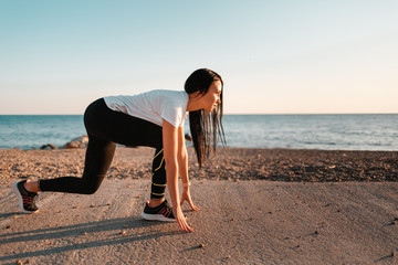 Sports and Jogging along the sea. A young brunette woman stands ready to run. In the background, the sea and the rocky shore.Copy space