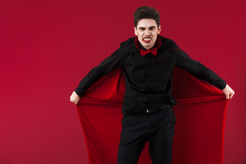 Image of angry vampire man in black halloween costume holding his cloak