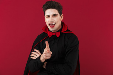 Image of happy vampire man in black halloween costume pointing finger