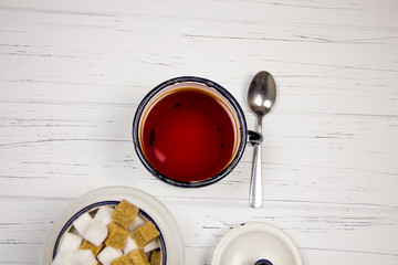 tea in a white enameled cup, cane sugar and white cubed sugar cubes in a sugar bowl tea spoon on a light wooden background