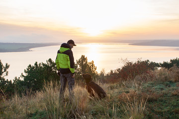 man with his labrador dog admiring orange sunrise over the lake
