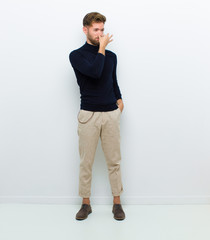 young full body man feeling disgusted, holding nose to avoid smelling a foul and unpleasant stench...
