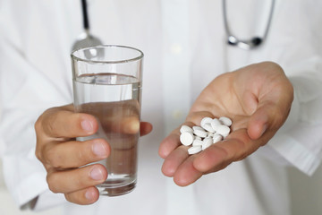 Pills and glass of water in hands of doctor, physician giving medication in white tablets. Concept of dose of drugs, medical exam, pharmacist, antibiotics or vitamins