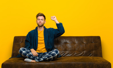 young man wearing pajamas feeling serious, strong and rebellious, raising fist up, protesting or...