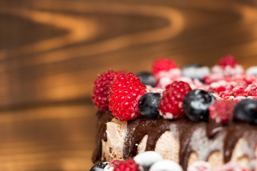 A close-up view of vegan chocolate cake covered with raspberries and blueberries, frozen in the refrigerator, on a table with blurred background. Copy space. Delicious healthy diet. Selective focus