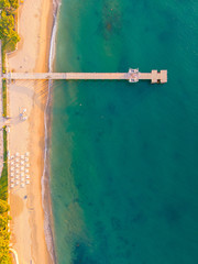 Aerial top view on the sandy beach. Umbrellas, sand, bridge and sea waves landscape.