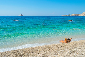 Fototapeta na wymiar A girl is lying on the beach enloying the view of turquoise waters of the ocean at Petani beach in Kefalonia, Greece