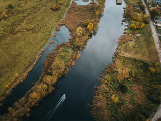 Aerial view of narrow river with small boat sailing by surrounded by autumn meadows - enjoy water sports concept
