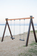 Simple children's wooden swings on an empty sandy beach