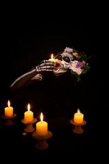 Woman in ghost bodypaint holding candle light in to her mouth on dark background