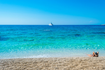 Fototapeta premium A girl is lying on the beach enloying the view of turquoise waters of the ocean at Petani beach in Kefalonia, Greece