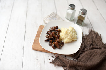 Sesame beef dish on a white wood background served with mashed potatoes and seasonings