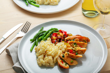 Two plates with baked chicken fillet, potato, green beans and vegetable sauce. Delicious meal with wine on a wooden table. Traditional healthy lunch for two people.