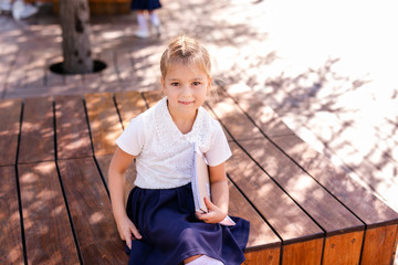 Little blonde girl in school uniform studying at the park