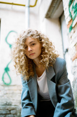 A young girl in a strict elegant gray suit is looking directly at the camera. Curly blonde sits on...