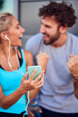 Modern woman and man jogging / exercising in urban surroundings and using cellphone at a pause / break.